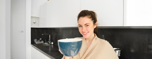 Free photo portrait of beautiful smiling young woman offering you morning cup of coffee extending her hand with