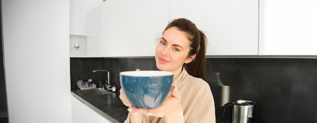 Free photo portrait of beautiful smiling young woman offering you morning cup of coffee extending her hand with