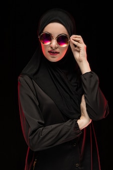Portrait of beautiful stylish young muslim woman wearing black hijab and sunglasses as modern eastern fashion concept posing
