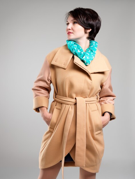 Портрет красивой женщины в бежевом осеннем пальто с зеленым шарфом