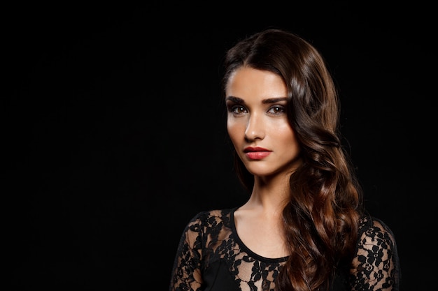 Portrait of beautiful woman in black dress over dark wall