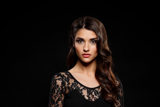 Portrait of beautiful woman in black dress over dark wall