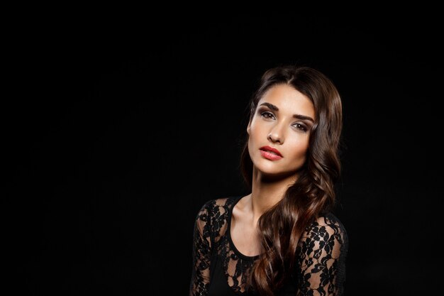 Portrait of beautiful woman in black dress over dark wall