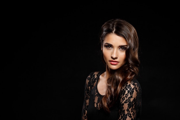 Portrait of beautiful woman in black dress over dark wall