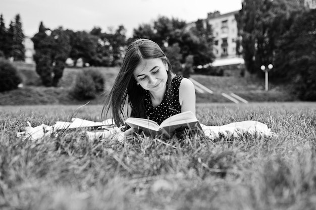 草の上の毛布の上に横たわって、白黒写真を読んでいる黒の水玉模様のドレスを着た美しい女性の肖像画