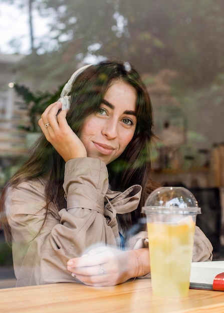 Portrait of beautiful woman in cafe with fresh lemonade and headphones