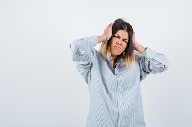 Portrait of beautiful woman clasping head with hands in shirt and looking annoyed front view