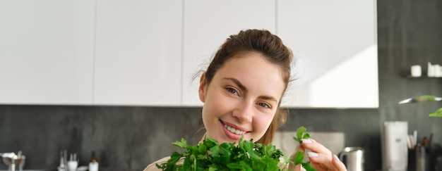 Portrait of beautiful woman cooking holding fresh parsley adding herbs while making salad healthy