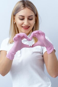 Portrait of a beautiful woman dentist looking at artificial tooth in hands. heart shape. stomatologist in white uniform.