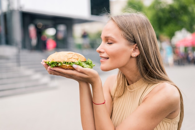 Portrait of beautiful woman eating tasty hamburger on the street