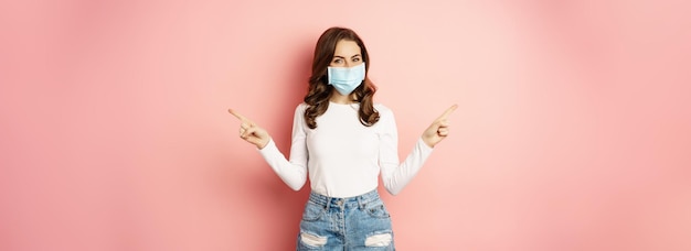 Free photo portrait of beautiful woman in face medical mask pointing sideways showing two choices ways sides de