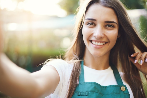 Foto gratuita ritratto di una bella donna giardiniera che si fa un selfie nel suo negozio di forniture da giardino