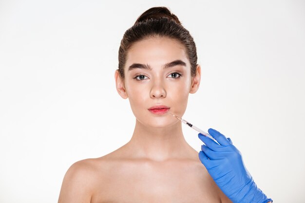 portrait of beautiful woman getting injection in her lips with botox having plastic surgery in clinic
