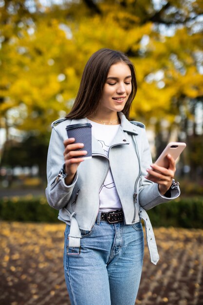 Portrait of beautiful woman holding coffee reading message in the park