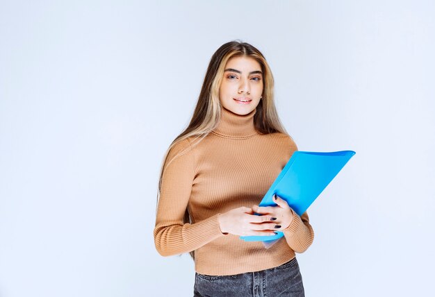 Portrait of a beautiful woman holding a folder against white wall .