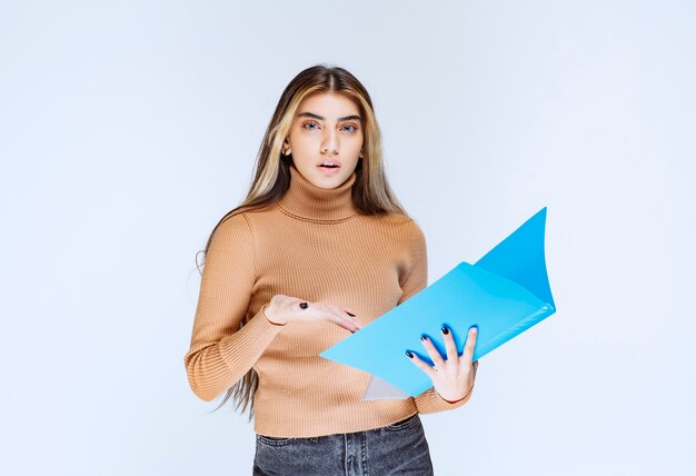 Portrait of a beautiful woman holding a folder against white wall .