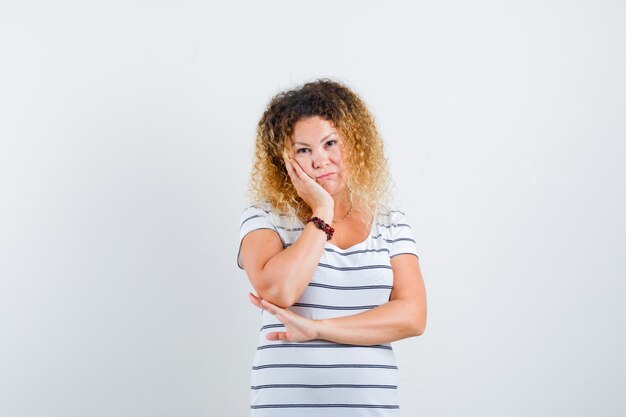 Portrait of beautiful woman holding hand on cheek in t-shirt and looking pensive front view