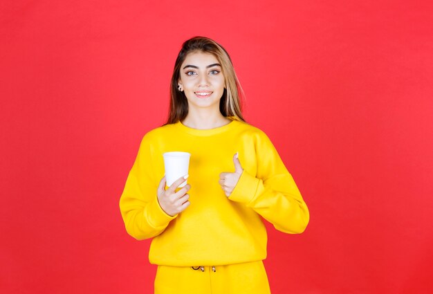 Portrait of beautiful woman holding plastic cup of tea and giving thumbs up