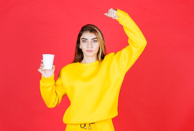 Portrait of beautiful woman holding plastic cup of tea on red wall