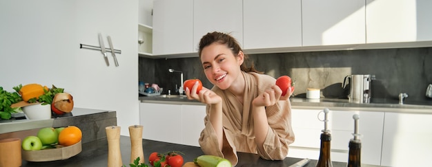 Foto gratuita ritratto di bella donna che tiene i pomodori in piedi in cucina in accappatoio e cucina