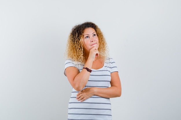 Portrait of beautiful woman keeping hand on chin in t-shirt and looking thoughtful front view