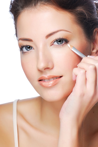 Portrait of beautiful woman making make-up using white eyeliner for eyes