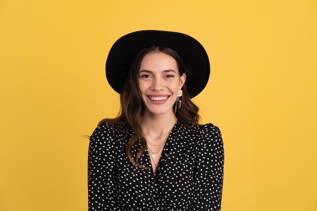 portrait of beautiful woman posing isolated on yellow wearing black dotted dress and black hat