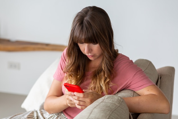 Foto gratuita ritratto di bella donna che si distende sul divano di casa. donna che tiene in mano uno smart phone.