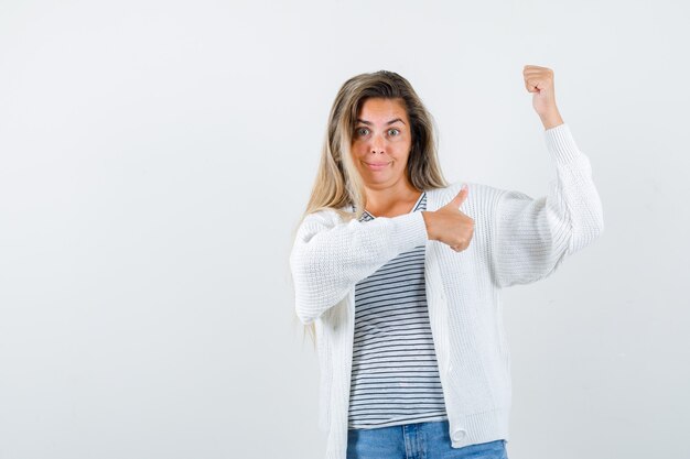 Portrait of beautiful woman showing winner gesture thumb up in jacket and looking pleased front view