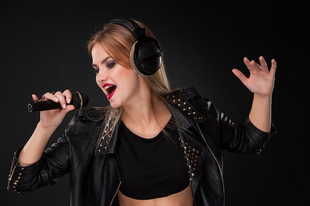 Portrait of a beautiful woman singing into microphone with headphones in  on black wall
