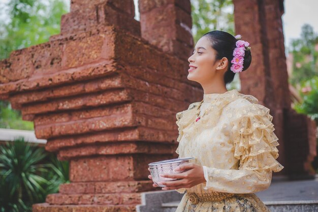 물 그릇을 들고 사원에서 태국 전통 의상을 입은 송크란 축제의 아름다운 여성 초상화와 물 축제와 함께 태국 문화 미소