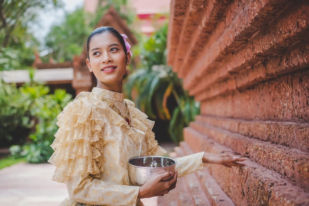 Ritratto di bella donna nel festival di songkran con il costume tradizionale tailandese nel tempio che tiene una ciotola d'acqua e un sorriso cultura thailandese con il festival dell'acqua