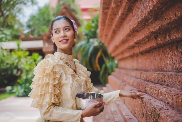 물 그릇을 들고 사원에서 태국 전통 의상을 입은 송크란 축제의 아름다운 여성 초상화와 물 축제와 함께 태국 문화 미소