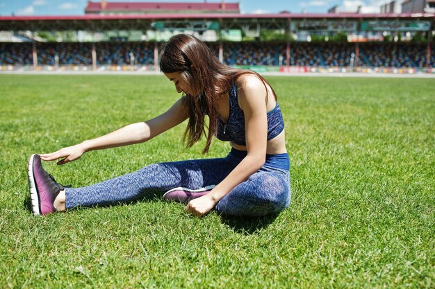 Portrait of a beautiful woman in sportswear stretching her muscles in the stadium