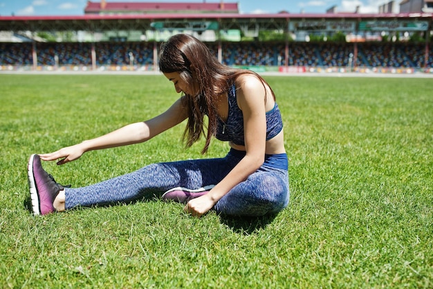 Portrait of a beautiful woman in sportswear stretching her muscles in the stadium