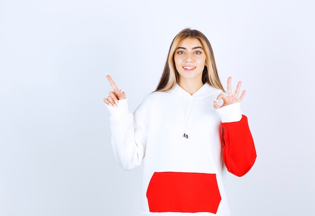 Portrait of a beautiful woman in warm hoodie pointing up and showing ok gesture