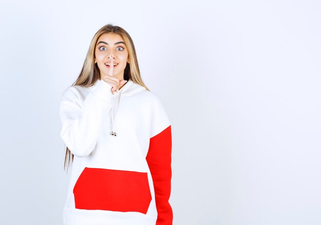 Portrait of a beautiful woman in warm hoodie standing and doing silent sign 