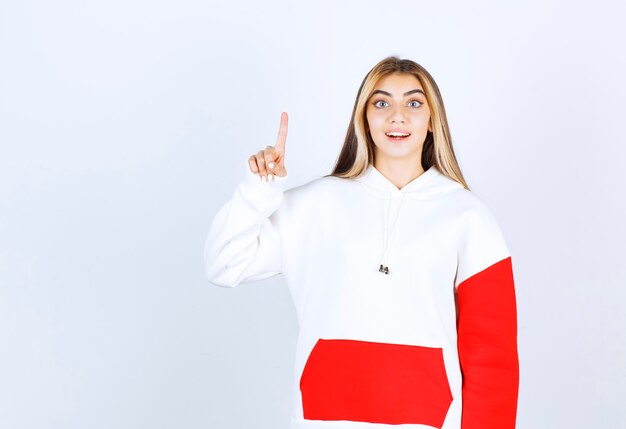 Portrait of a beautiful woman in warm hoodie standing and pointing up