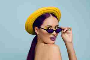 Free photo portrait of beautiful woman with bright make-up, hat and sunglasses on blue studio