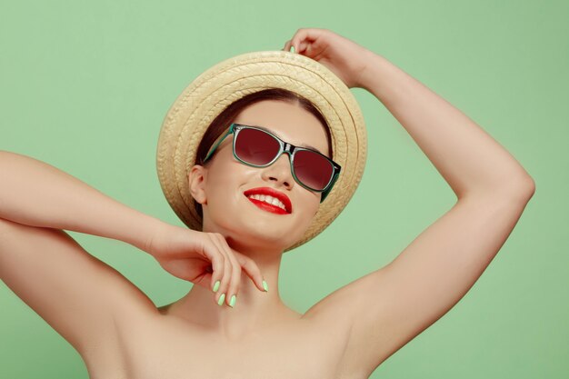 Portrait of beautiful woman with bright make-up, hat and sunglasses on green studio