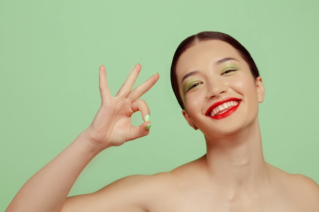 Portrait of beautiful woman with bright make-up, red eyewear and hat on green  space. Stylish and fashionable make, hairstyle