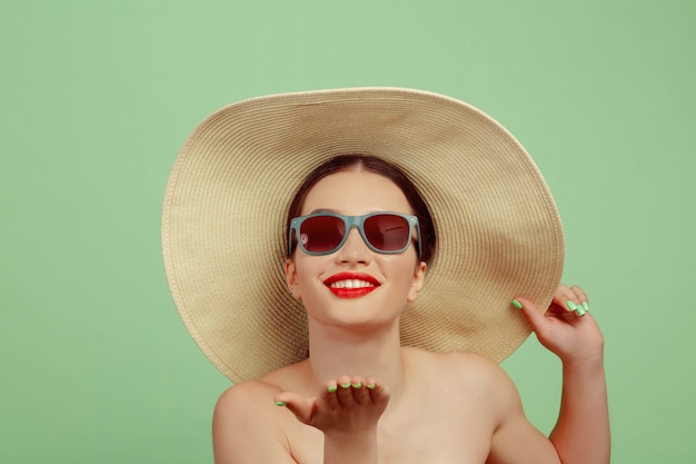 Portrait of beautiful woman with bright make-up, red eyewear and hat on green studio