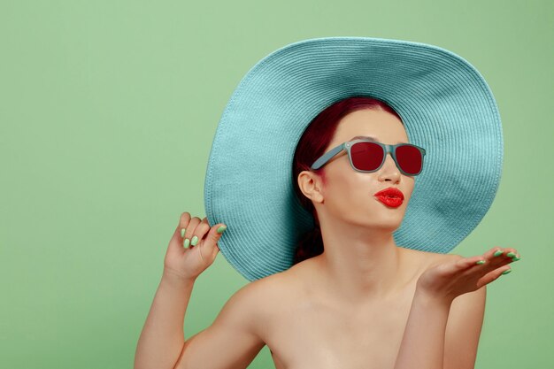 Portrait of beautiful woman with bright make-up, red eyewear and hat on green studio