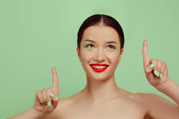 Portrait of beautiful woman with bright make-up, red eyewear and hat on green studio