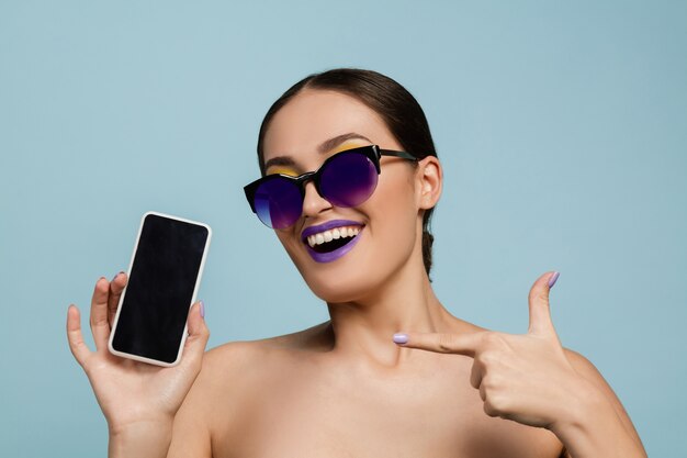 Portrait of beautiful woman with bright make-up and sunglasses on blue studio