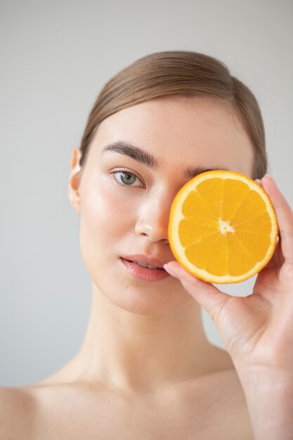 スライスしたオレンジ色の果物を保持している透明な肌を持つ美しい女性の肖像画