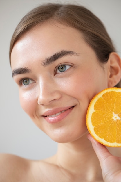 スライスしたオレンジ色の果物を保持している透明な肌を持つ美しい女性の肖像画