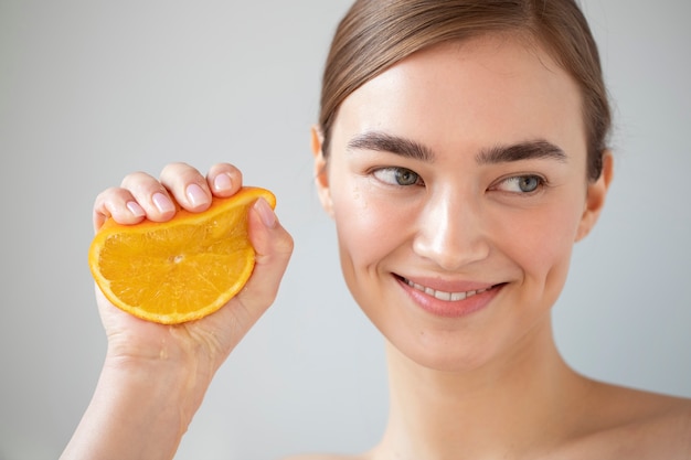 Portrait of beautiful woman with clear skin holding sliced orange fruit