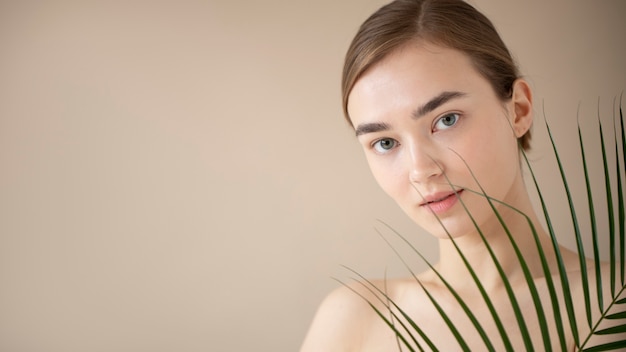 Portrait of beautiful woman with clear skin posing with leaf and copy space