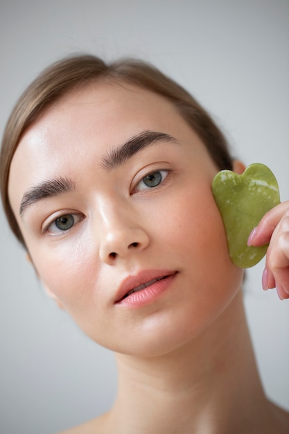 Portrait of beautiful woman with clear skin using guasha to massage her face